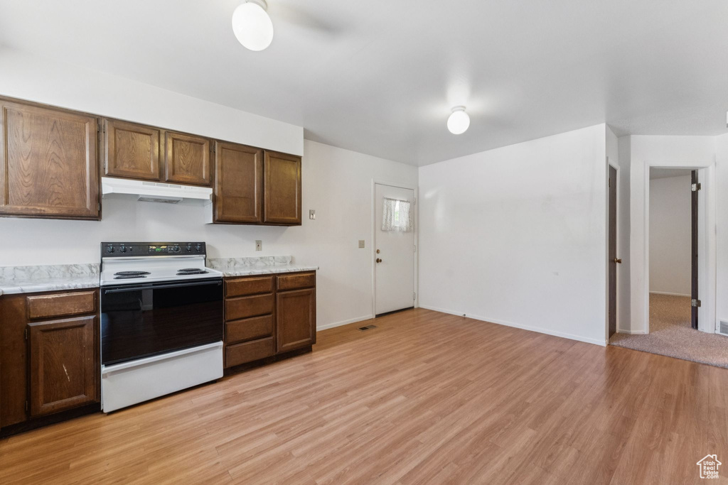 Kitchen with white electric range, under cabinet range hood, light countertops, and light wood-style flooring