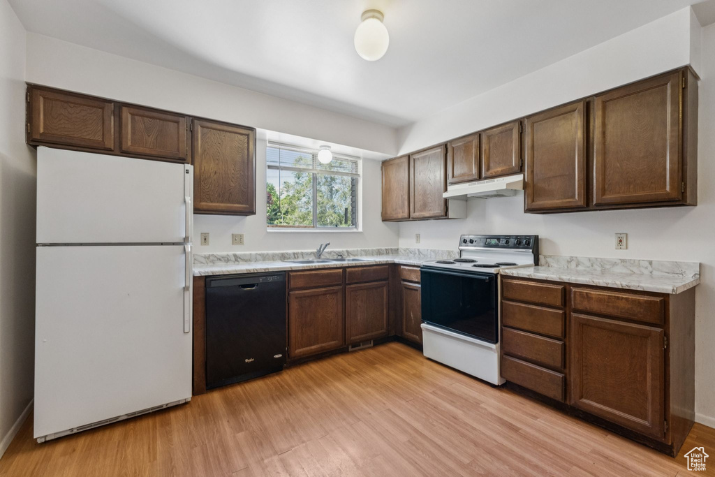 Kitchen with white appliances, under cabinet range hood, light wood-style floors, light countertops, and dark brown cabinetry