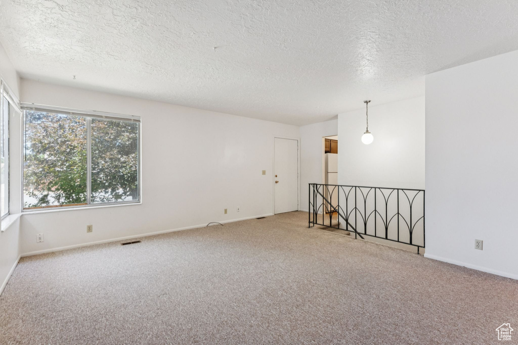 Carpeted empty room with a textured ceiling and baseboards