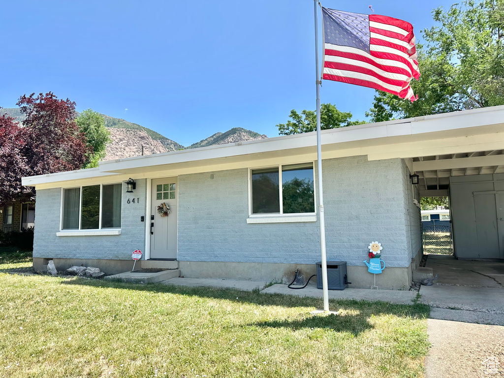 View of front of property with a front yard, brick siding, a mountain view, entry steps, and a carport