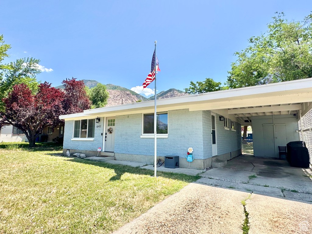 Ranch-style house with driveway, brick siding, a front yard, a mountain view, and a carport