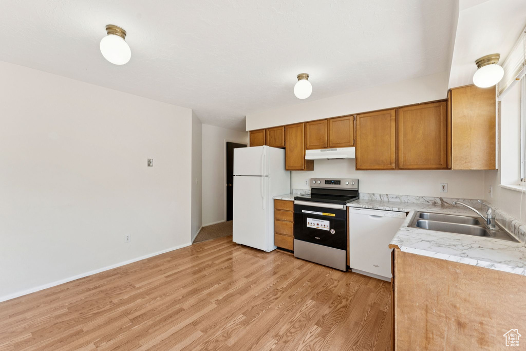 Kitchen with white appliances, under cabinet range hood, light wood finished floors, light countertops, and brown cabinets