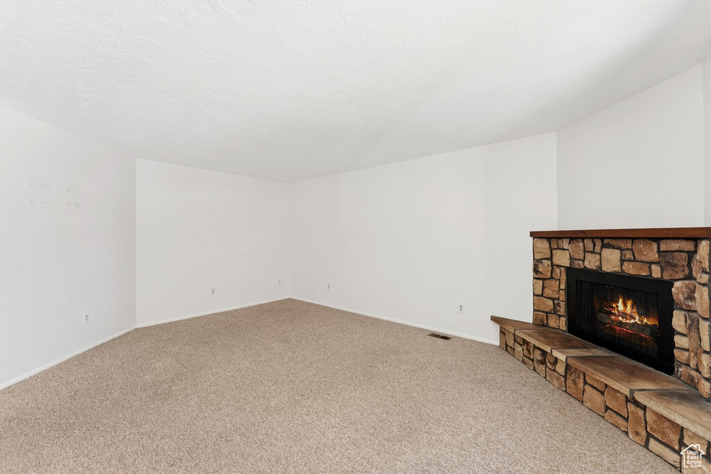 Unfurnished living room with carpet flooring and a stone fireplace
