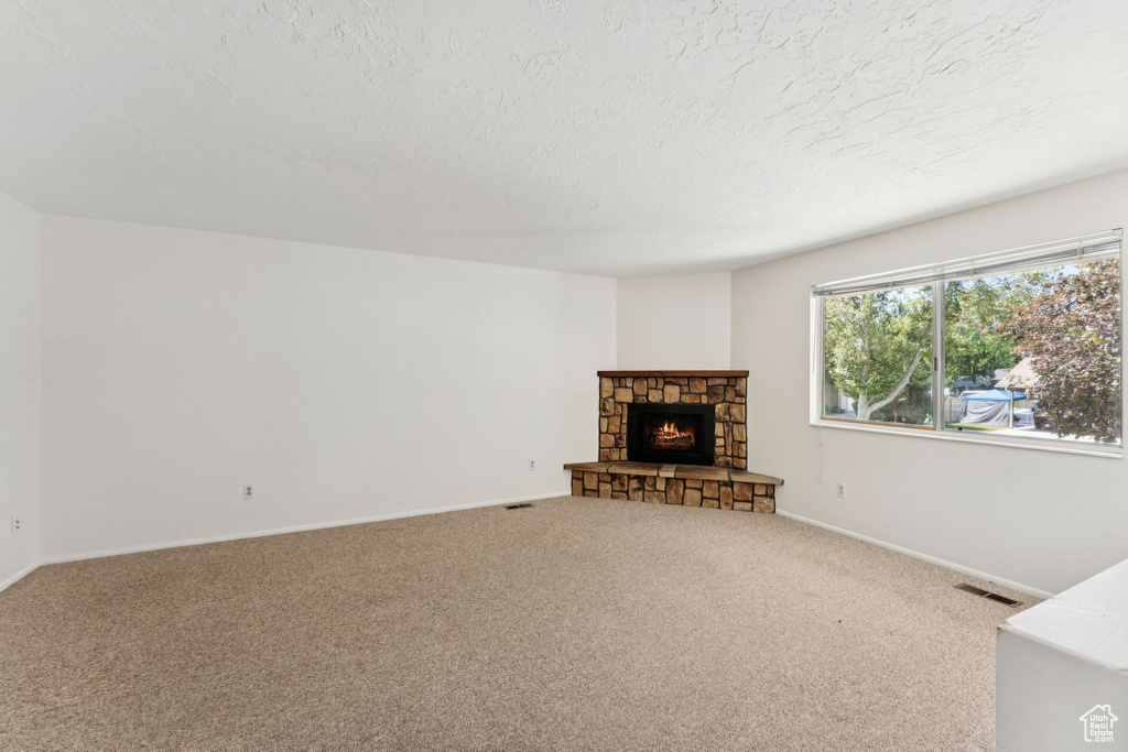 Unfurnished living room with carpet flooring, a textured ceiling, and a fireplace