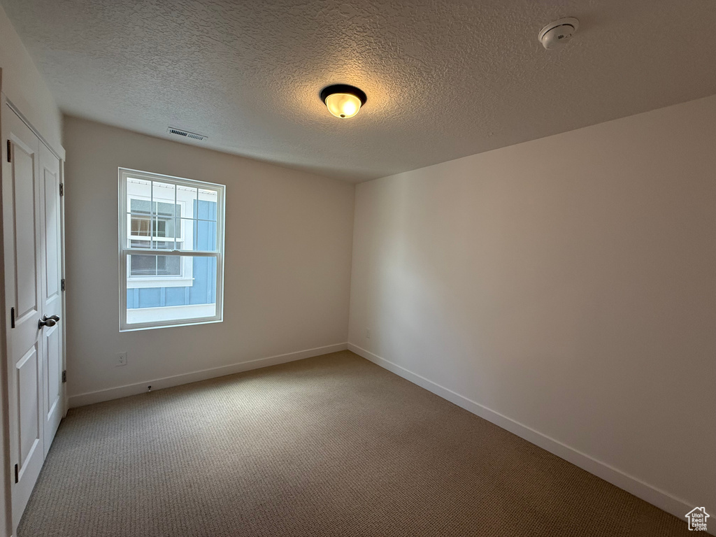 Carpeted spare room featuring a smoke detector and a textured ceiling