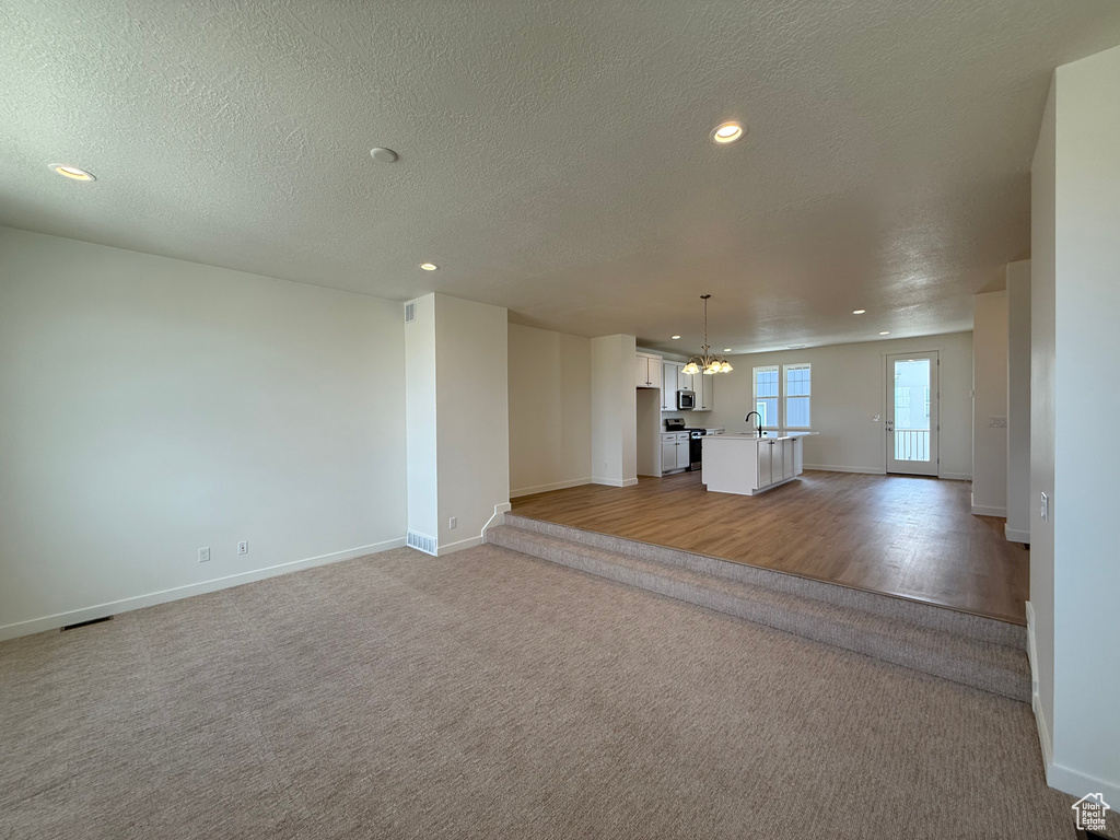 Unfurnished living room with a chandelier, light carpet, recessed lighting, and a textured ceiling