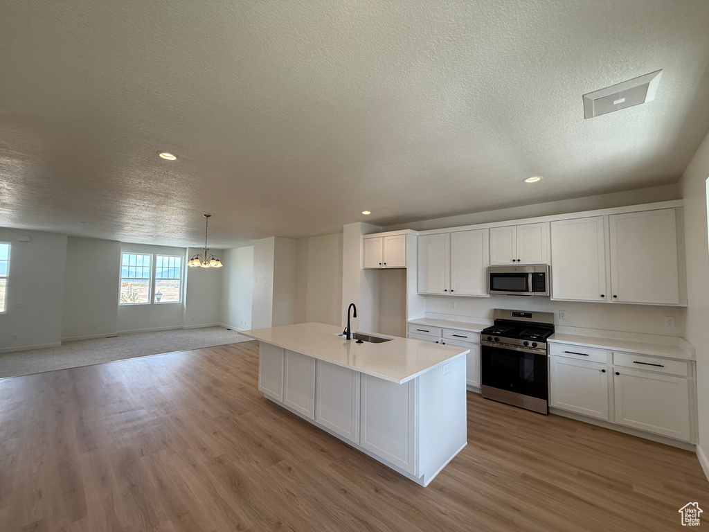 Kitchen featuring appliances with stainless steel finishes, a chandelier, a textured ceiling, light wood-type flooring, and white cabinetry