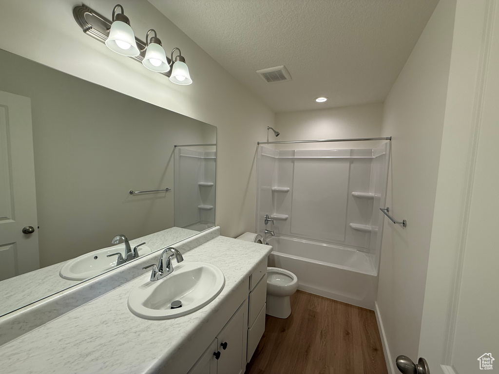Bathroom with vanity, wood finished floors, shower / bath combination, and a textured ceiling