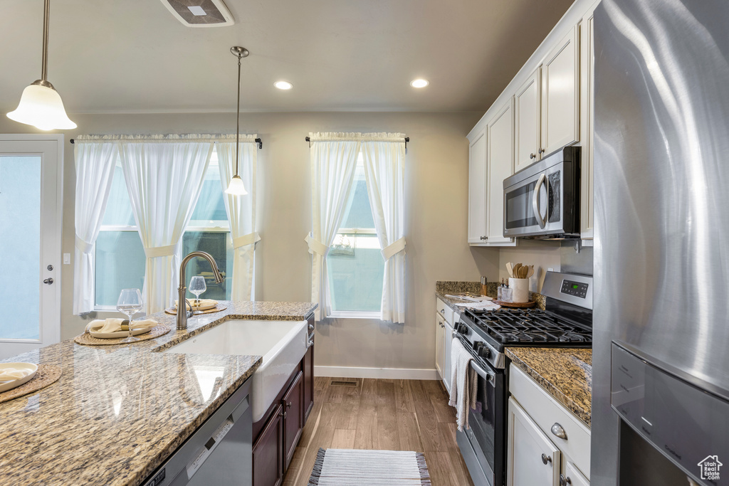 Kitchen with stainless steel appliances, wood finished floors, white cabinetry, decorative light fixtures, and recessed lighting