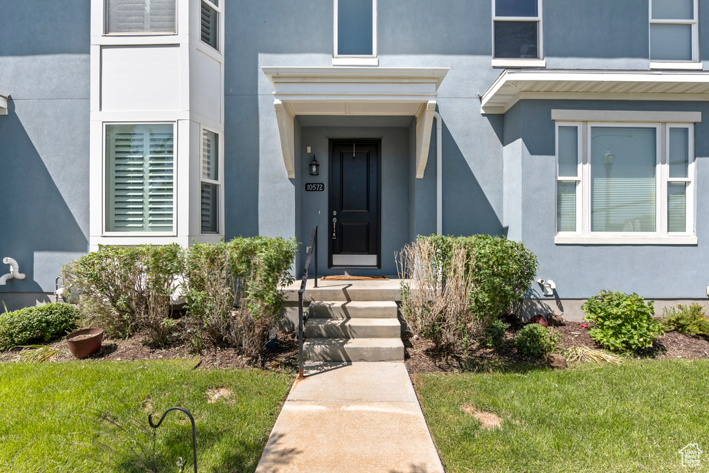 View of exterior entry with stucco siding and a yard