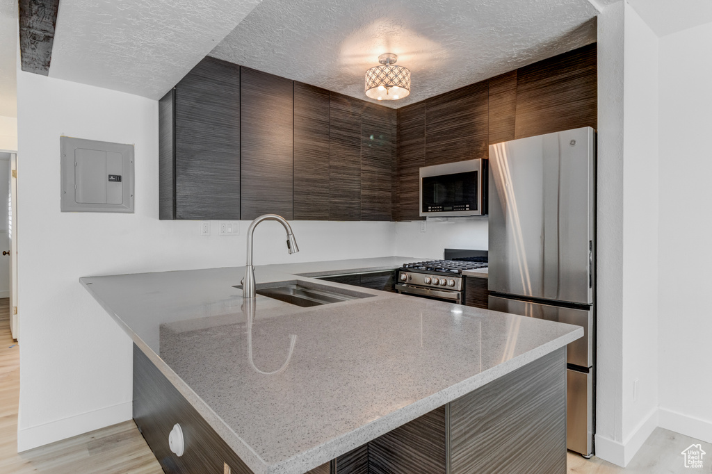 Kitchen featuring appliances with stainless steel finishes, electric panel, modern cabinets, a peninsula, and light wood-style floors