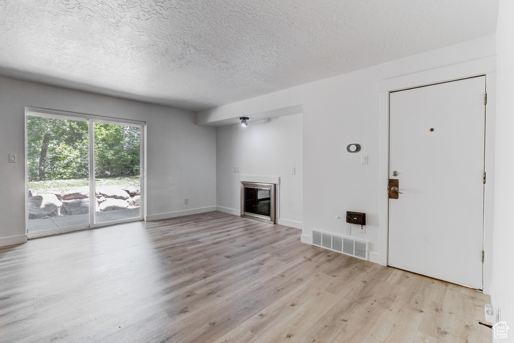 Unfurnished living room with light wood-type flooring, a glass covered fireplace, and a textured ceiling