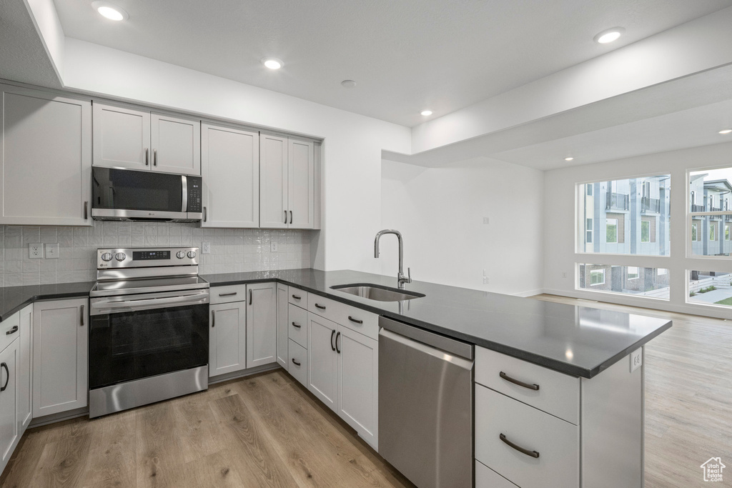 Kitchen with appliances with stainless steel finishes, a peninsula, dark countertops, light wood-type flooring, and recessed lighting