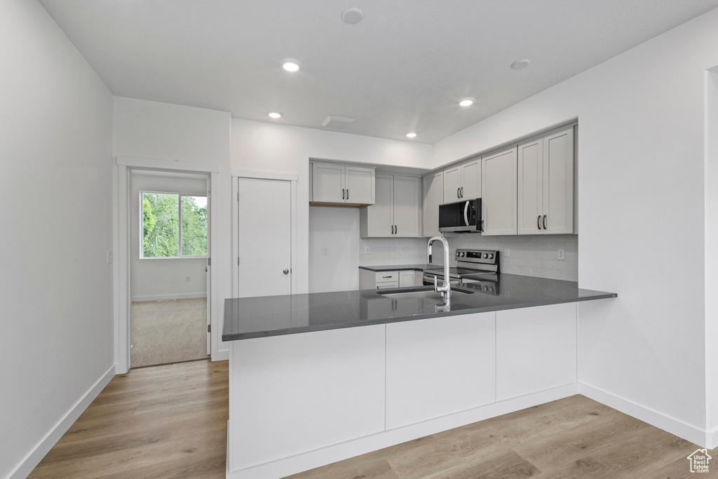 Kitchen featuring stainless steel appliances, a peninsula, dark countertops, tasteful backsplash, and light wood finished floors