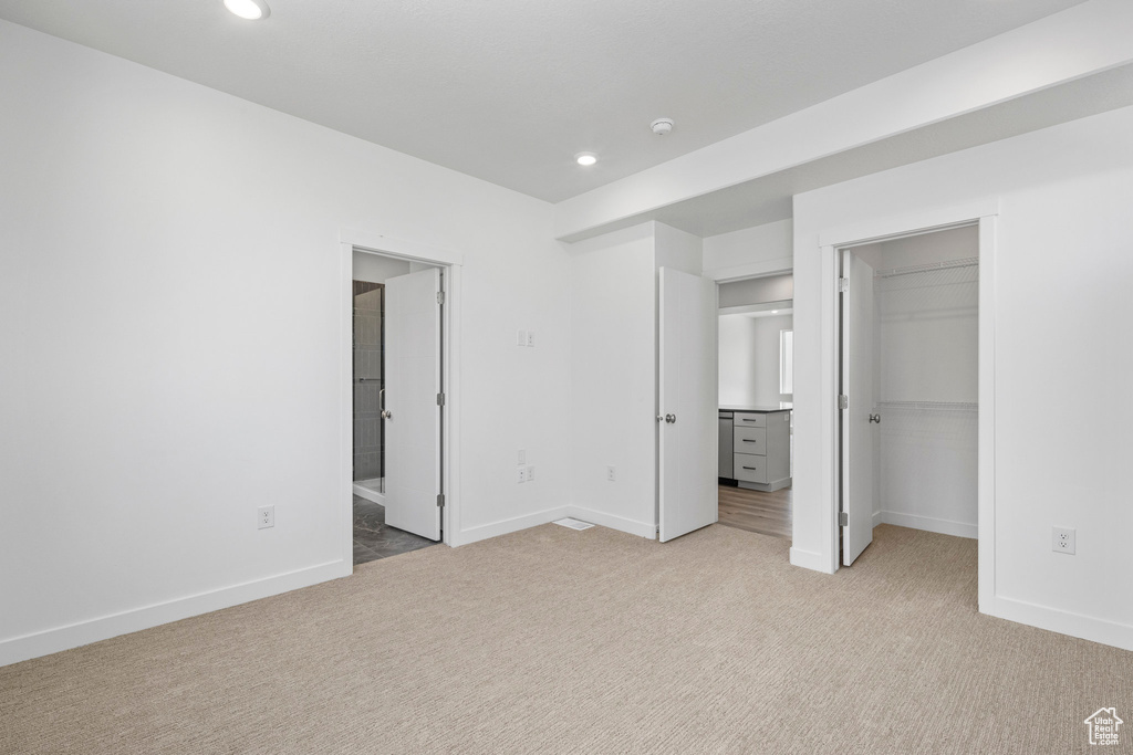 Unfurnished bedroom with light colored carpet, recessed lighting, a walk in closet, connected bathroom, and a closet