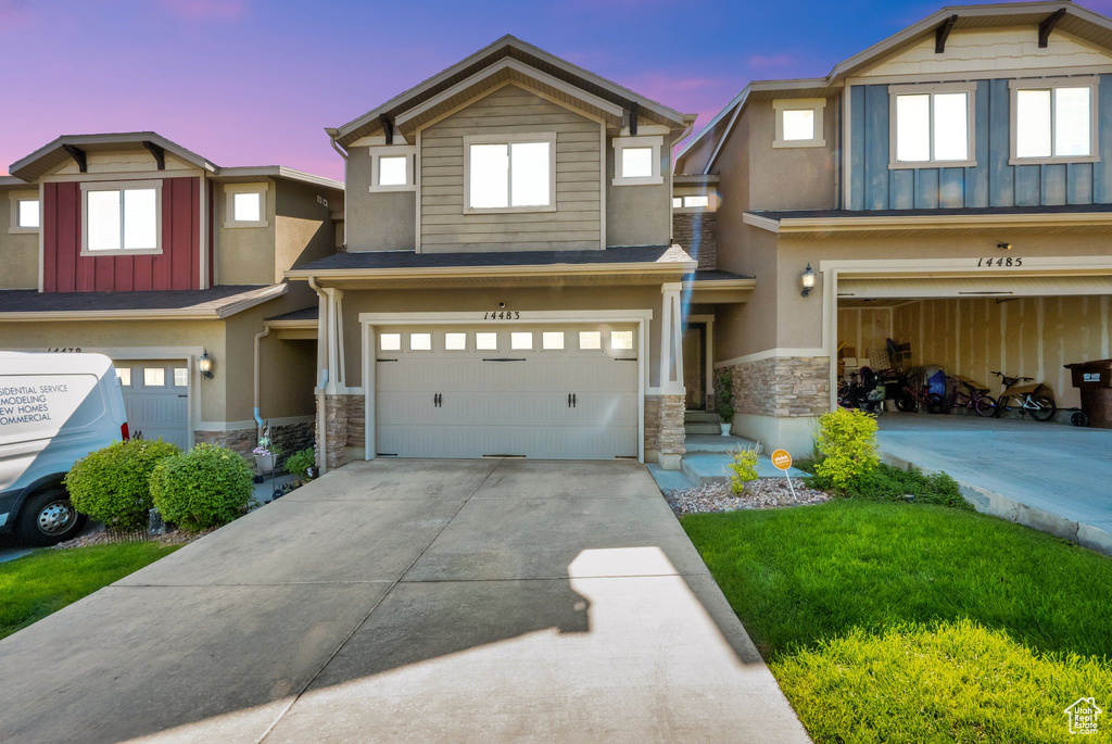 View of front of property featuring stone siding, an attached garage, driveway, board and batten siding, and stucco siding