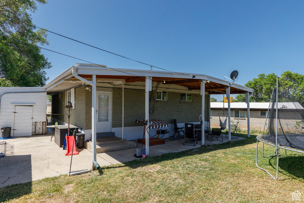 Rear view of property with a trampoline, a patio, a yard, brick siding, and a storage unit
