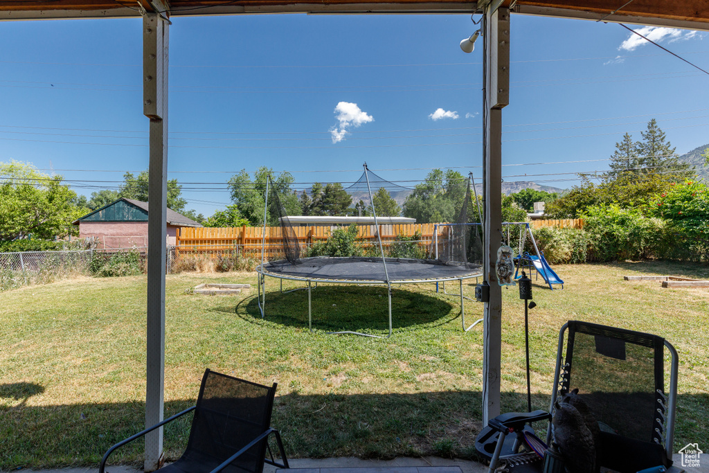 Fenced backyard featuring a trampoline and a playground