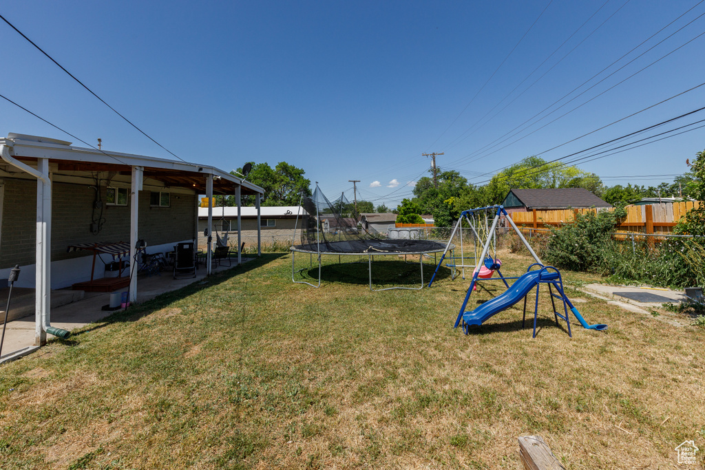 Fenced backyard featuring a trampoline, a playground, and a patio