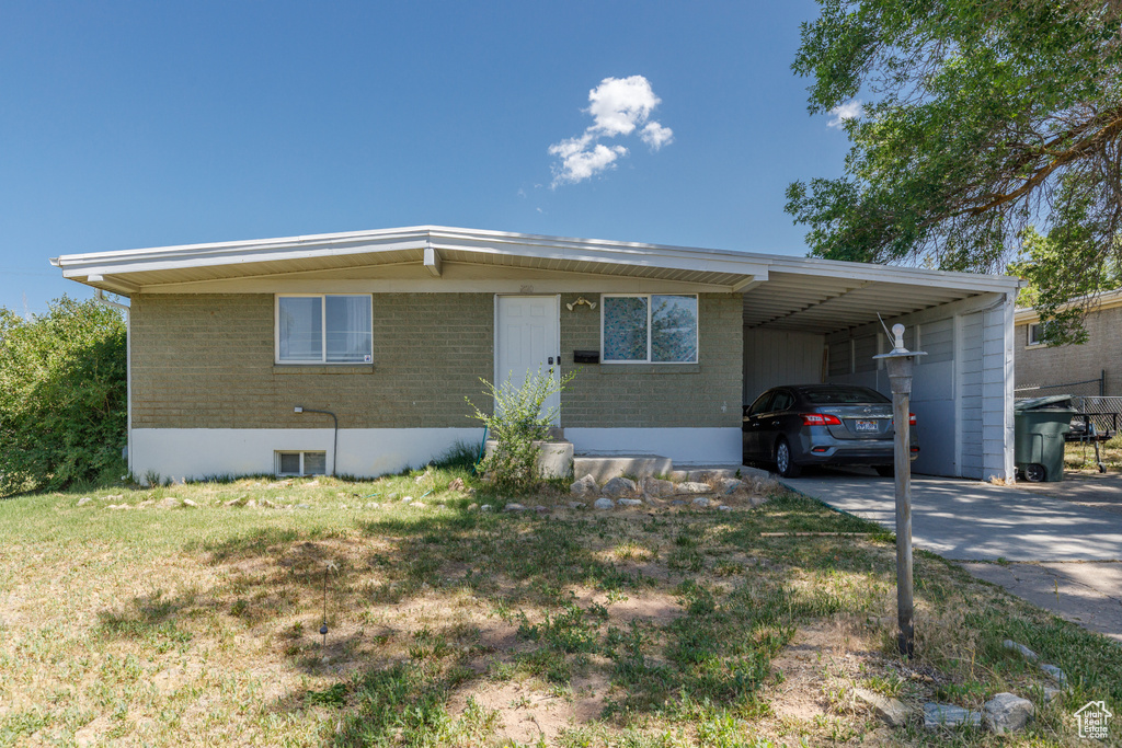 View of front facade featuring an attached carport, driveway, brick siding, and a front yard
