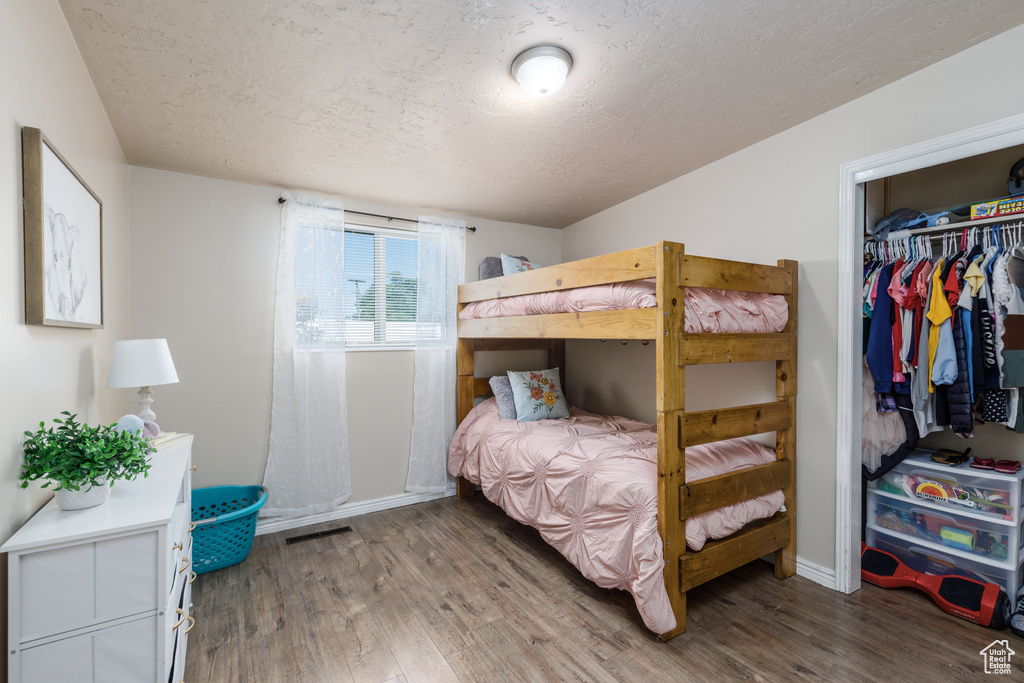 Bedroom with a textured ceiling, wood finished floors, and a closet