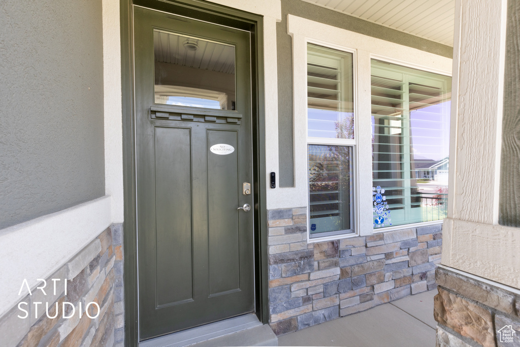 View of exterior entry featuring covered porch, stone siding, and stucco siding