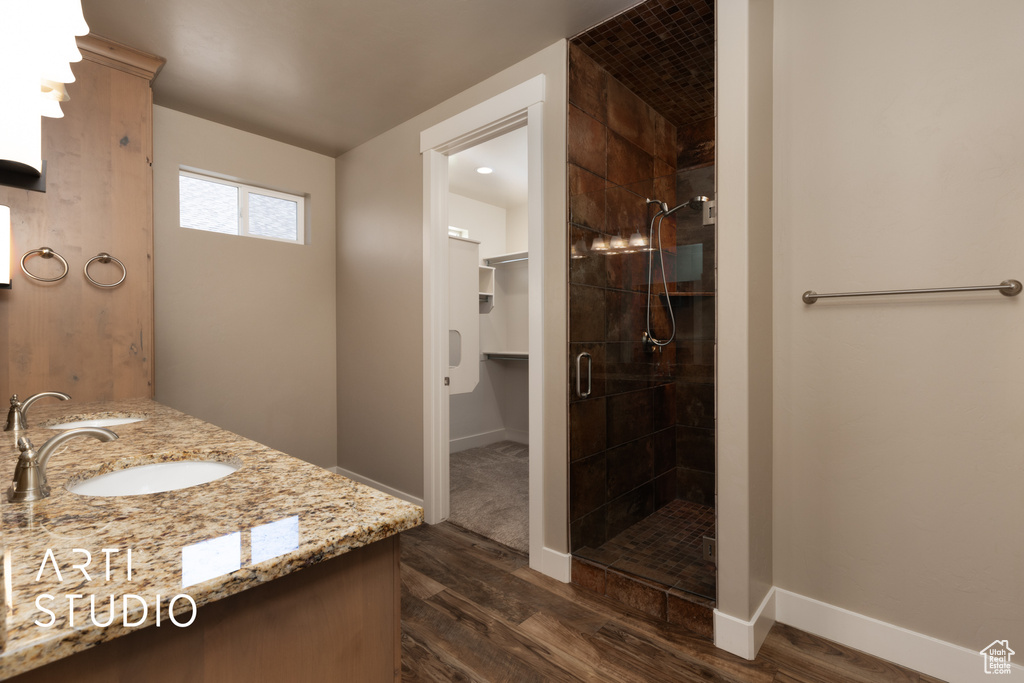 Bathroom featuring wood finished floors, a shower stall, double vanity, and a walk in closet