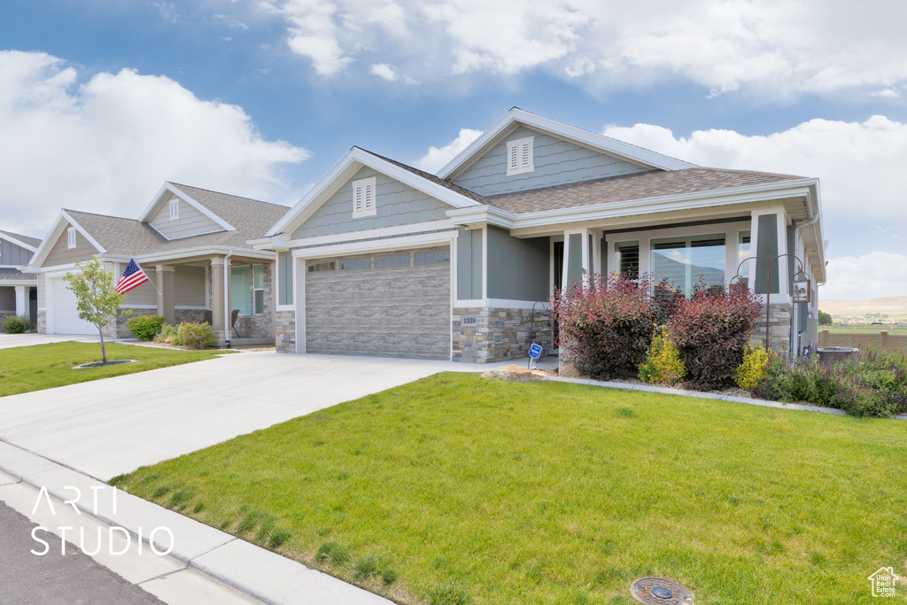 Craftsman-style home featuring stone siding, a front yard, a garage, and concrete driveway