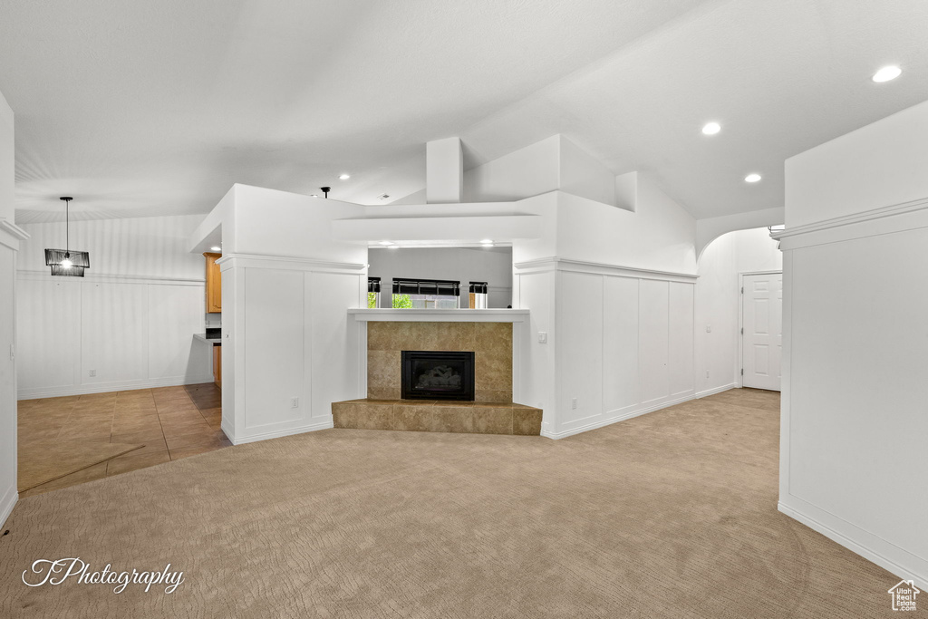 Unfurnished living room featuring light carpet, a decorative wall, recessed lighting, a tiled fireplace, and lofted ceiling