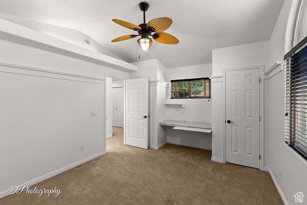 Unfurnished bedroom featuring vaulted ceiling, carpet floors, an office area, and a ceiling fan