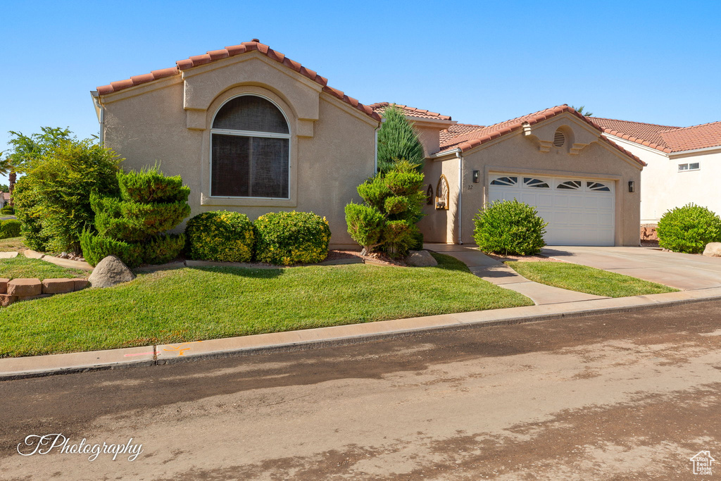 Mediterranean / spanish-style house featuring a tiled roof, an attached garage, a front yard, concrete driveway, and stucco siding