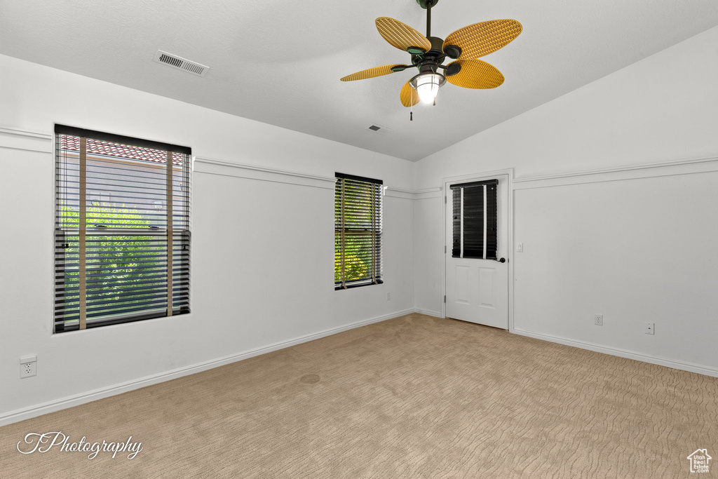 Empty room featuring ceiling fan, lofted ceiling, and carpet floors