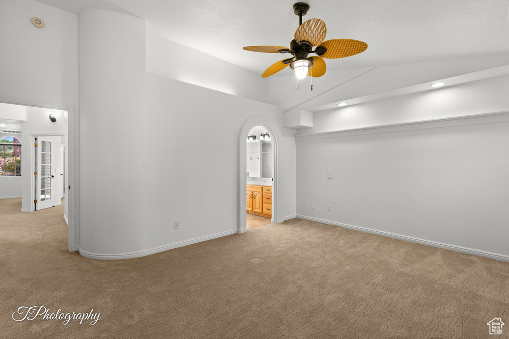 Empty room with light carpet, high vaulted ceiling, a ceiling fan, and arched walkways