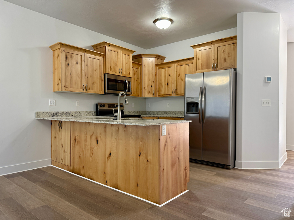 Kitchen featuring stainless steel appliances, a peninsula, wood finished floors, and light stone countertops