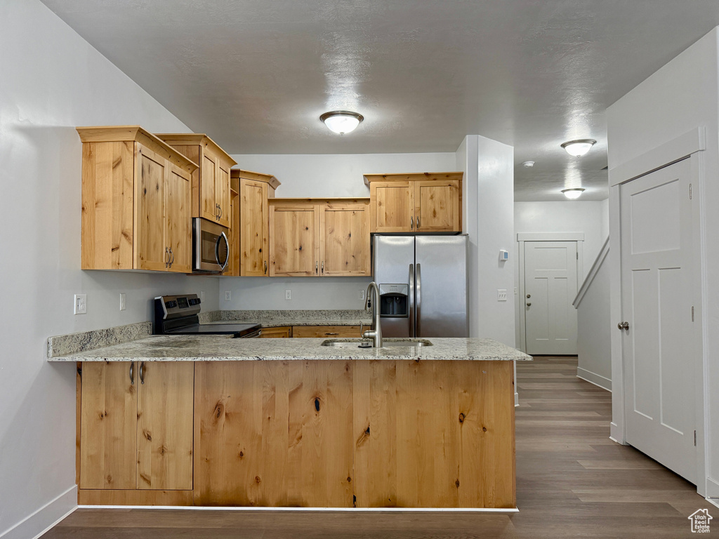 Kitchen featuring stainless steel appliances, a peninsula, dark wood-style flooring, and light stone countertops