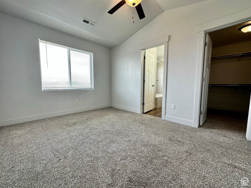 Unfurnished bedroom featuring lofted ceiling, carpet flooring, a walk in closet, a closet, and connected bathroom