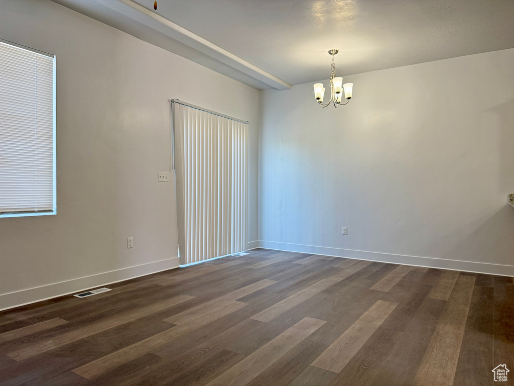 Empty room featuring a chandelier and dark wood-type flooring