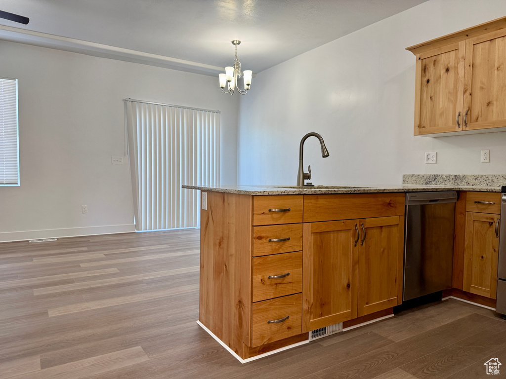 Kitchen with stainless steel dishwasher, wood finished floors, a peninsula, light stone countertops, and a chandelier