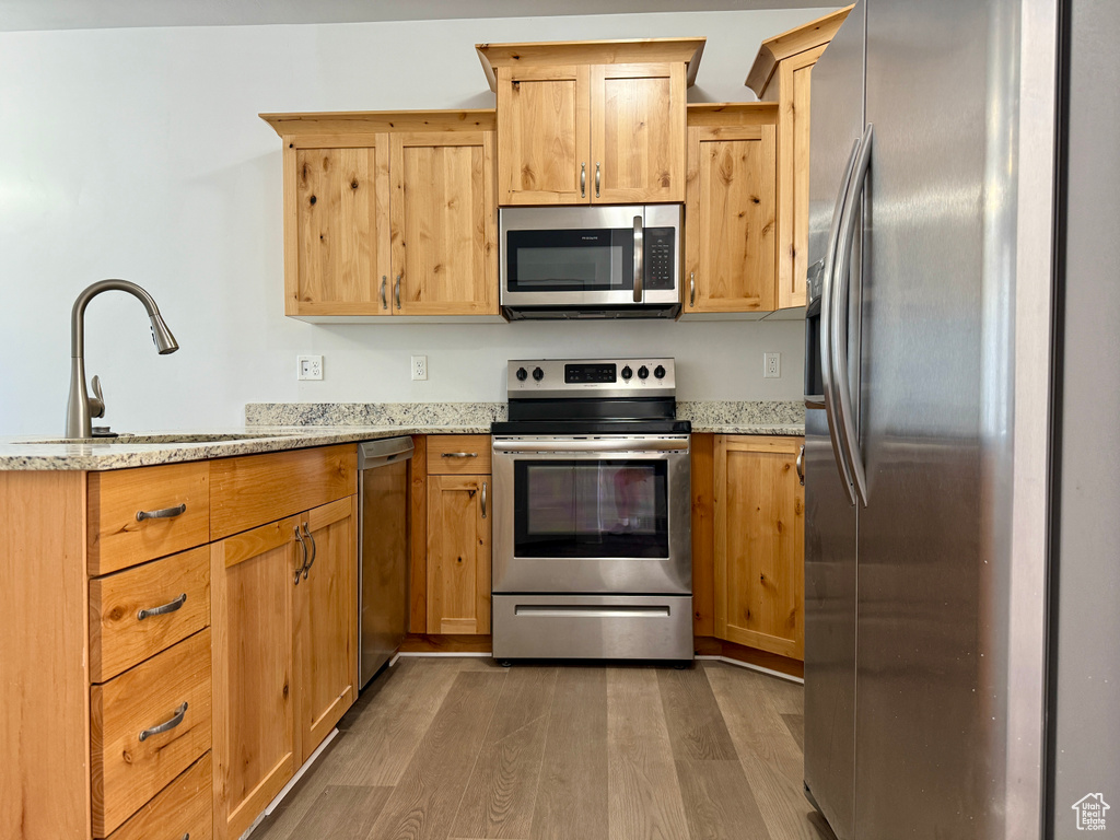 Kitchen featuring stainless steel appliances, a peninsula, wood finished floors, light stone countertops, and light brown cabinetry