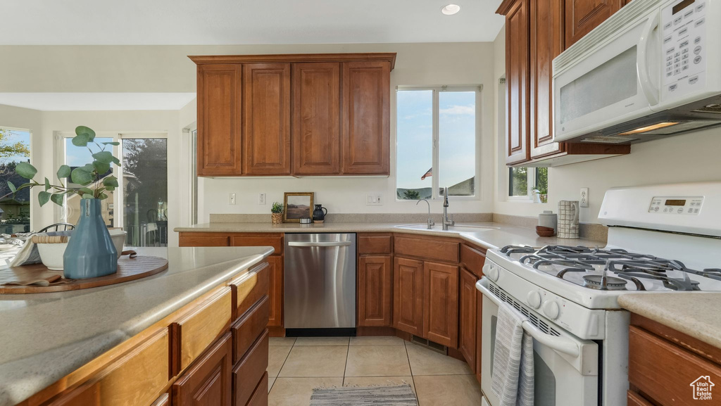 Kitchen with white appliances, light tile patterned flooring, brown cabinetry, and light countertops