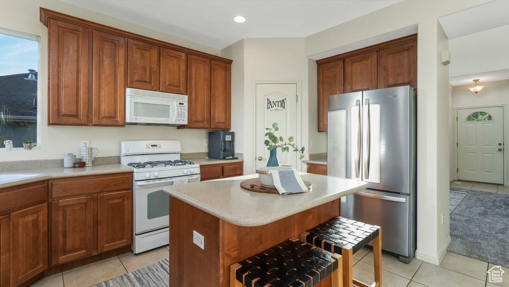 Kitchen with white appliances, light tile patterned floors, light countertops, a center island, and a breakfast bar