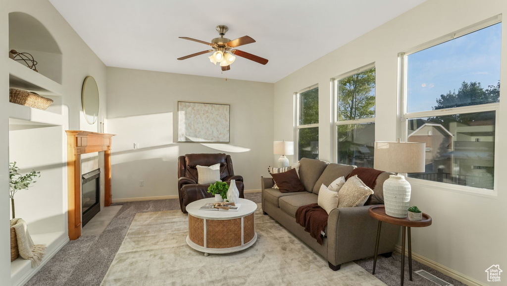 Living area with a glass covered fireplace, light colored carpet, and a ceiling fan