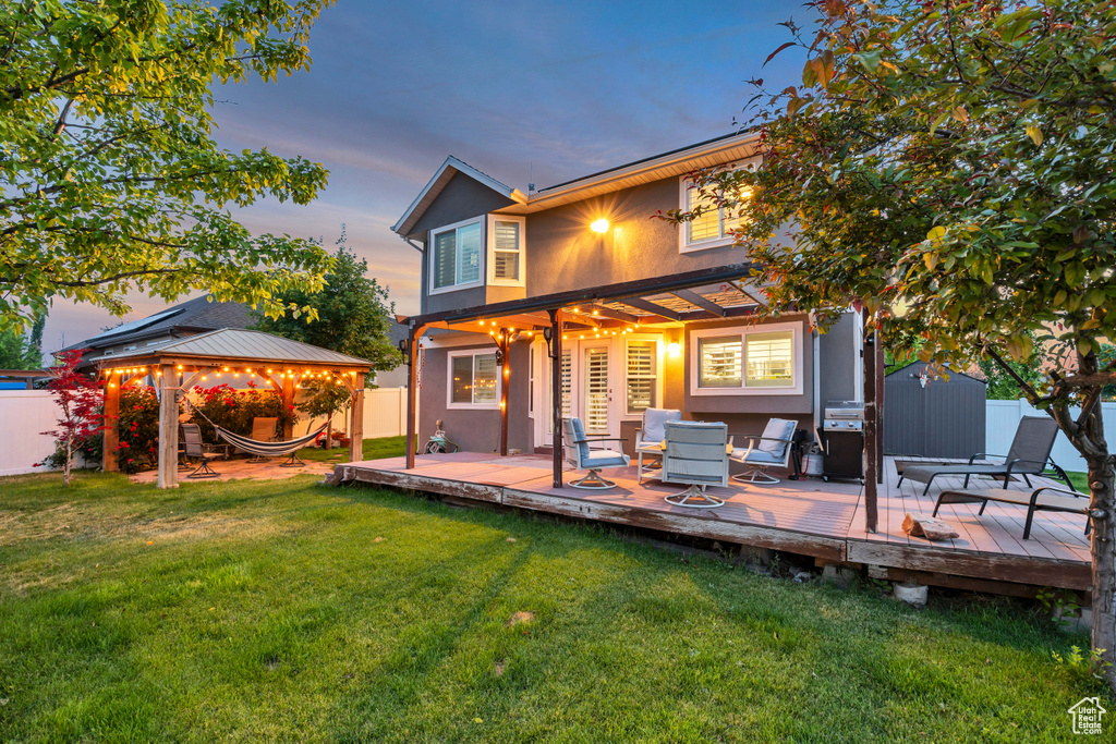 Back of house at dusk with a gazebo, a fenced backyard, stucco siding, a deck, and an outdoor hangout area