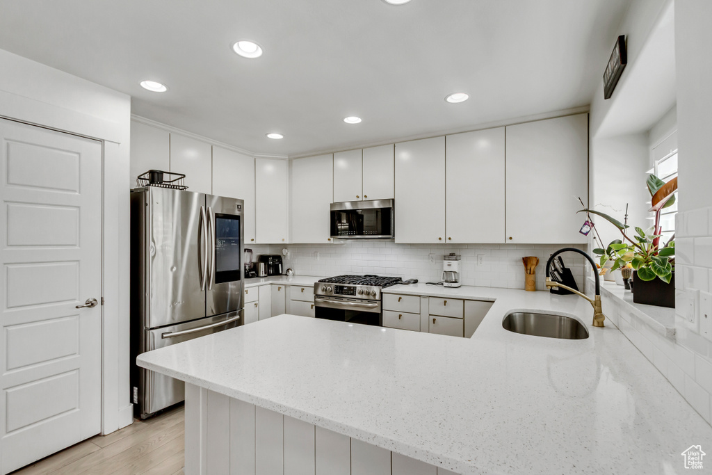Kitchen with appliances with stainless steel finishes, a peninsula, tasteful backsplash, light stone countertops, and recessed lighting