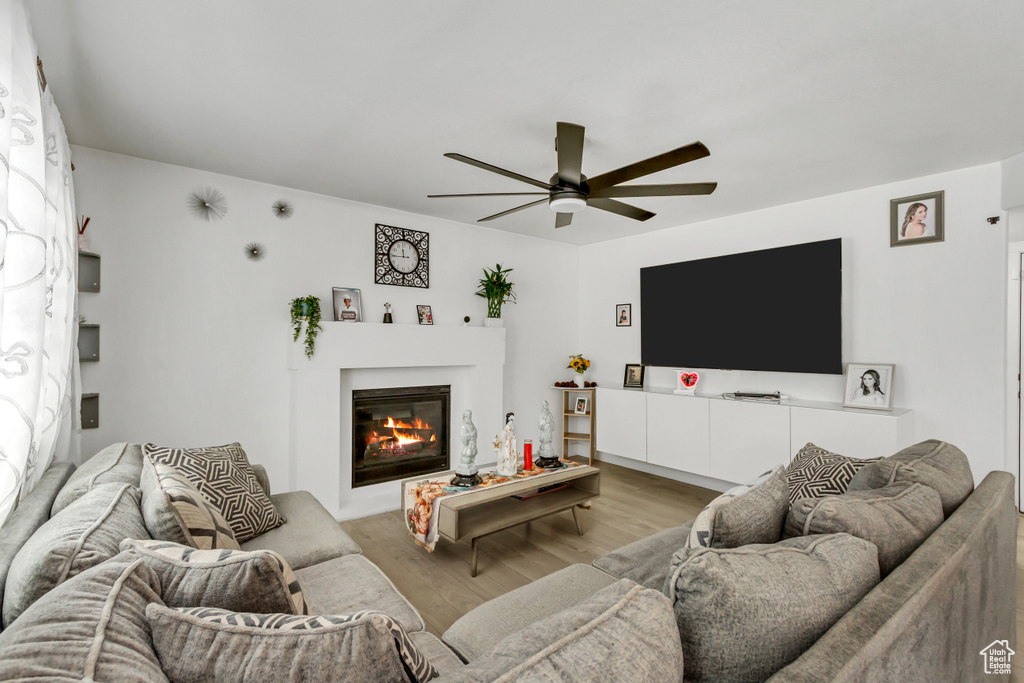Living area with ceiling fan, light wood-type flooring, and a glass covered fireplace