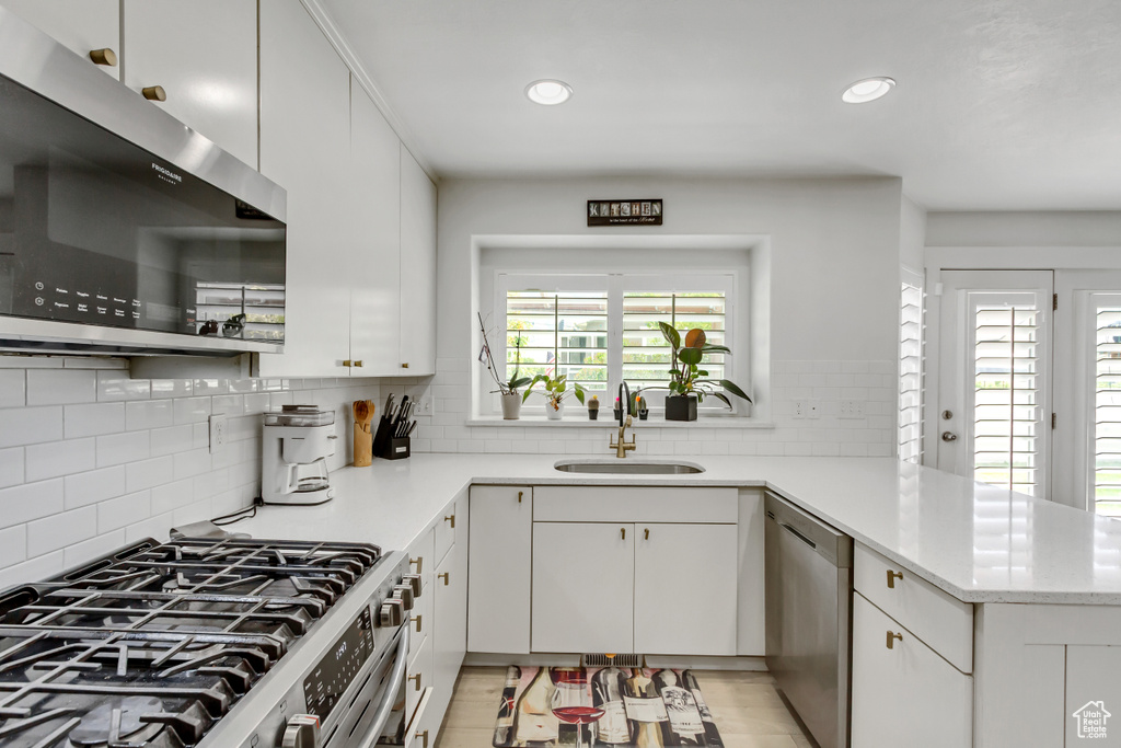 Kitchen with stainless steel appliances, a peninsula, recessed lighting, decorative backsplash, and white cabinetry