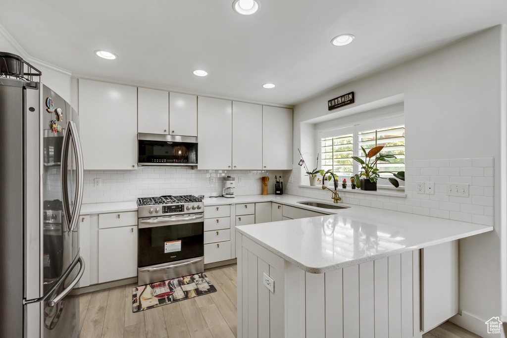 Kitchen with stainless steel appliances, a peninsula, light countertops, decorative backsplash, and light wood finished floors