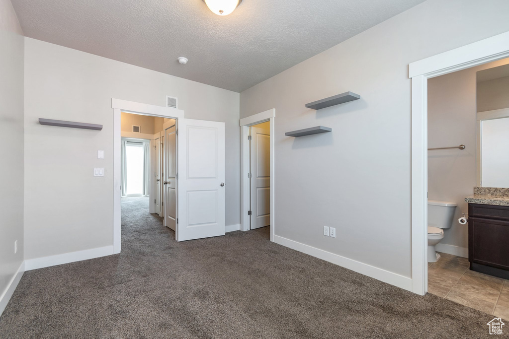 Unfurnished bedroom featuring carpet floors, ensuite bathroom, and a textured ceiling