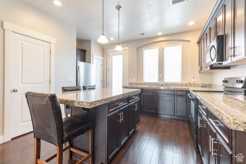 Kitchen with stainless steel appliances, a kitchen bar, a center island, recessed lighting, and decorative light fixtures