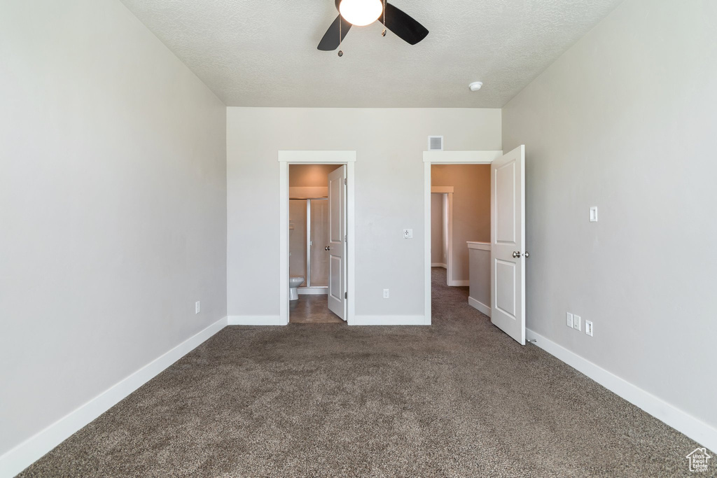 Unfurnished bedroom featuring dark colored carpet, ensuite bathroom, ceiling fan, and a textured ceiling